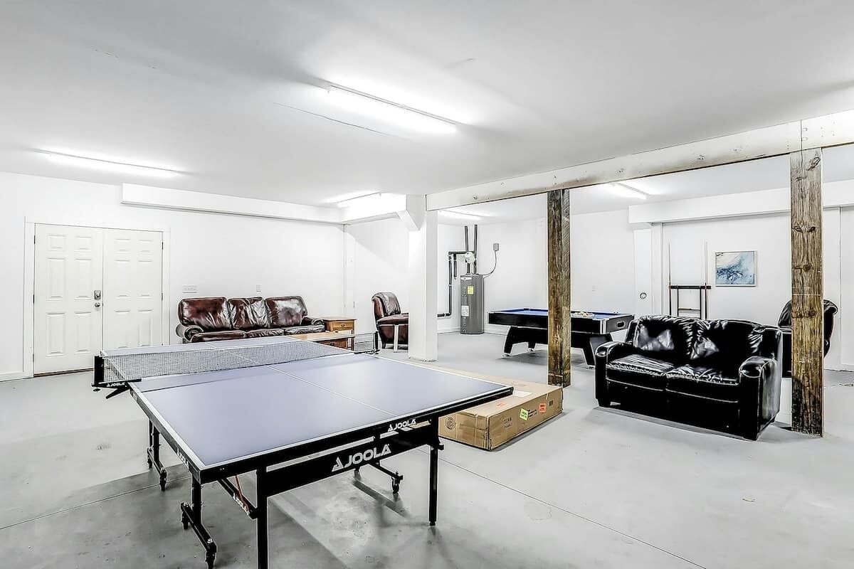 A spacious room with a ping pong table, a sofa, a pool table, and a billiards table.