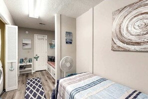 A bedroom with a bed, a fan, a door, and a wall with a circular design. - Waccamaw Condo - Unit 6 (Murrells Inlet)
