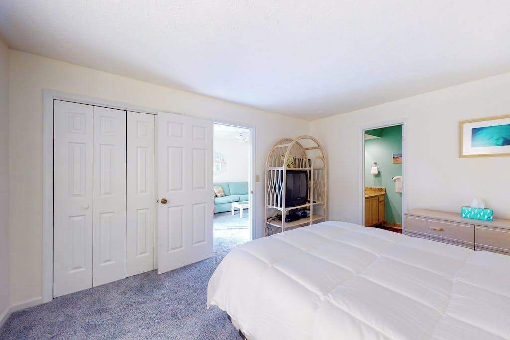 A bedroom with a bed, a television on a stand, a wardrobe, and a bathroom visible through an open door.