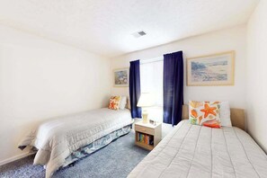 Quarto com duas camas de solteiro, mesa de cabeceira com abajur e janela com cortinas.