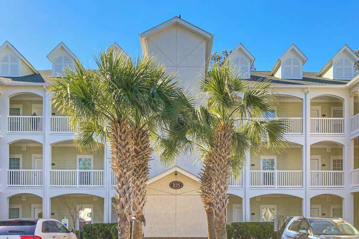A multi-story hotel with balconies, palm trees, and a clear sky.