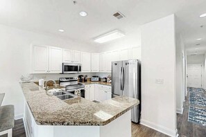 Une cuisine moderne avec des meubles blancs, des appareils en acier inoxydable et un plan de travail en granit.