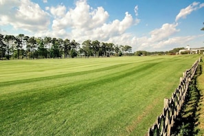 A golf course with a wooden fence, trees, and a building in the background. - World Tour Sawgrass 205 (Myrtle Beach)