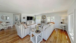 A spacious living room with a sofa, a television, and a dining area with chairs and a table. - Lands End Beach Retreat (Murrells Inlet)
