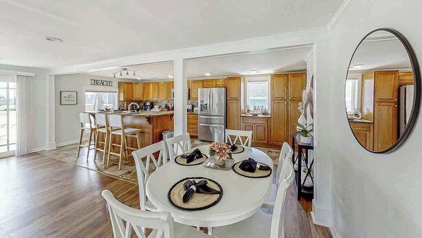 A spacious dining area with a white table and chairs, a kitchen with wooden cabinets, and a large mirror on the wall. - Lands End Beach Retreat (Murrells Inlet)
