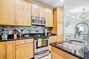 A kitchen with wooden cabinets, a stainless steel microwave, a stove, and a sink. - Windy Lane Leisure Retreat (Pawleys Island)