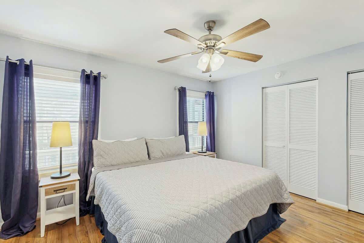 A bedroom with a bed, nightstands, a ceiling fan, and a window with curtains.