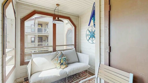 A room with a white sofa, a patterned rug, a ceiling fan, and a view of a balcony with a railing. - Dunes Pointe Unit B-11 (Myrtle Beach)