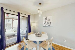 A room with a round table, chairs, a lamp, a sign on the wall, and a view through a glass door. - Dunes Pointe Unit B-11 (Myrtle Beach)