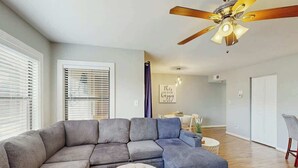 A living room with a sectional sofa, a round ottoman, a ceiling fan, and a dining area in the background. - Dunes Pointe Unit B-11 (Myrtle Beach)