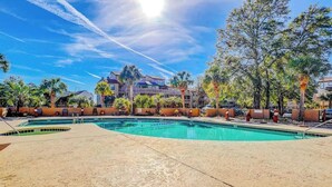 A swimming pool area with a clear sky, palm trees, and a building in the background. - Dunes Pointe Unit B-11 (Myrtle Beach)