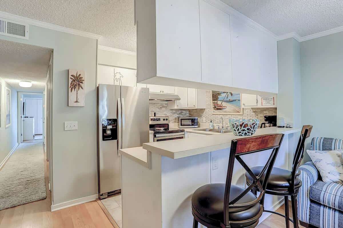 A modern kitchen with white cabinetry, a built-in microwave, and a central island with bar stools.