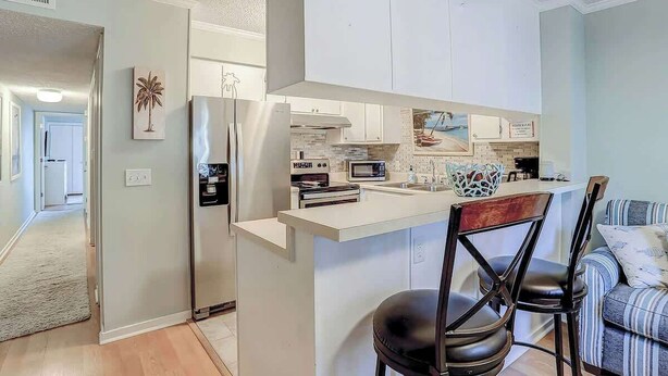 Een moderne keuken met witte kastjes, een ingebouwde magnetron en een centraal eiland met barstoelen.