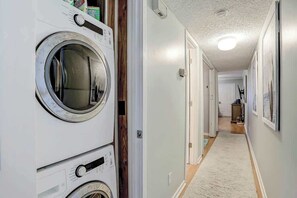 A laundry room with stacked washers and dryers, a hallway leading to a kitchen, and a white door at the end. - Toby Ct Unit A202 Condo (North Myrtle Beach)