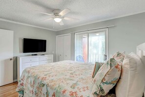 A bedroom with a bed, a television, a ceiling fan, and a sliding door to a balcony. - Toby Ct Unit A202 Condo (North Myrtle Beach)