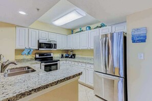 Una cocina con armarios blancos, un refrigerador de acero inoxidable, un microondas y una encimera de granito.