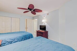 Ein Schlafzimmer mit zwei Betten, einem Deckenventilator, einem Fernseher auf einer Holzkommode und weißen Türen.