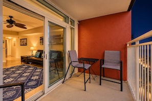 Ein Balkon mit Glastür zu einem Wohnzimmer, Deckenventilator und einer roten Wand.