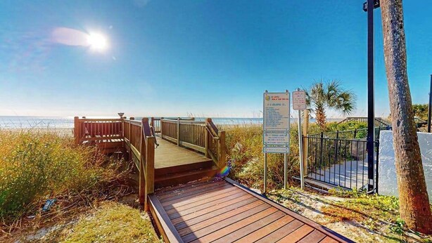 A wooden boardwalk leading to a beach with palm trees and a clear sky. - Beach Blessing Retreat (Myrtle Beach)