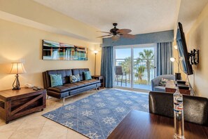 Una sala de estar con sofá, mesa de centro, lámpara, televisor y balcón con vistas.