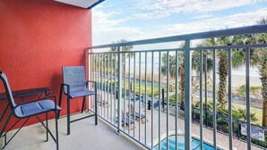 A balcony with a red wall, two chairs, and a view of a pool and palm trees. - Beach Blessing Retreat (Myrtle Beach)