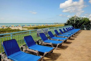 A beachside lounge with blue chairs and a sign indicating shallow water and no lifeguard on duty. - Roxanne Towers Unit PH1 (Myrtle Beach)