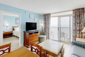 Ein Hotelzimmer mit Balkon, Fernseher, Esstisch und einer Couch.