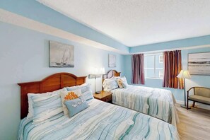 Ein Hotelzimmer mit zwei Betten, einem Holzkopfteil, einem Fenster mit Vorhängen und Bildern an den Wänden.
