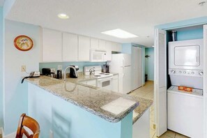 A compact kitchen with white cabinets, a granite countertop, a microwave, a stove, and a built-in oven. - Roxanne Towers Unit PH1 (Myrtle Beach)