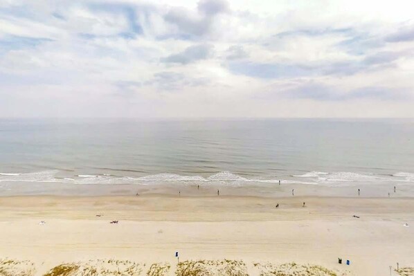 A beach with a clear sky, calm sea, and a sandy shore. - Roxanne Towers Unit PH1 (Myrtle Beach)