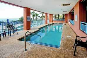 An indoor swimming pool with a view of the beach, surrounded by palm trees and equipped with lounge chairs. - Roxanne Towers Unit PH1 (Myrtle Beach)