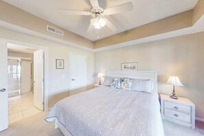 Ein Schlafzimmer mit Bett, Nachttischen, Deckenventilator und einer Tür zu einem anderen Raum.
