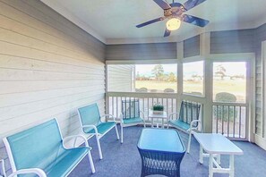 A covered porch with seating and a ceiling fan, overlooking a grassy area. - Tidewater Retreat Condo (North Myrtle Beach)