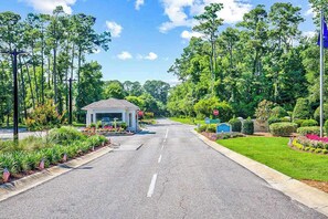 A road leading to a building with a covered entrance, surrounded by greenery and American flags. - Tidewater Retreat Condo (North Myrtle Beach)