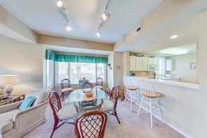 A dining area with a glass table and chairs, a sofa, and a kitchen in the background. - Tidewater Retreat Condo (North Myrtle Beach)
