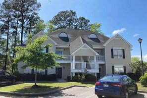 A two-story residential building with a balcony, a parking lot, and a tree in the foreground. - Scotch Broom Unit I-102 (Little River)