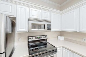 A kitchen with white cabinetry, a stainless steel refrigerator, a microwave, and an oven. - Scotch Broom Unit I-102 (Little River)