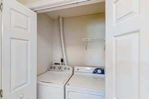 A laundry room with two stacked washers and dryers, a vent, and a small shelf. - Scotch Broom Unit I-102 (Little River)