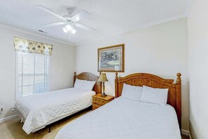 A bedroom with two single beds, a ceiling fan, a nightstand with a lamp, and a window with blinds. - Scotch Broom Unit I-102 (Little River)