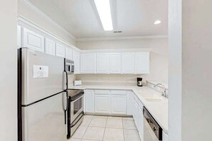 Eine Küche mit weißen Schränken, einem Edelstahlkühlschrank, einem eingebauten Backofen und einem Geschirrspüler.