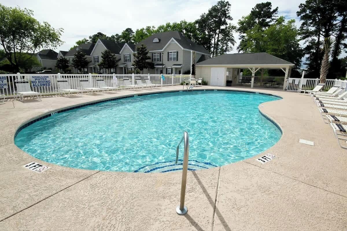 A swimming pool with a shallow end, a lifeguard stand, and a covered seating area.