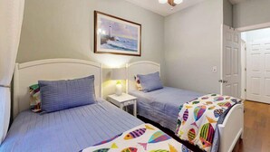 Ein Zimmer mit zwei Betten, einem Deckenventilator, einem gerahmten Bild an der Wand und einer Tür.
