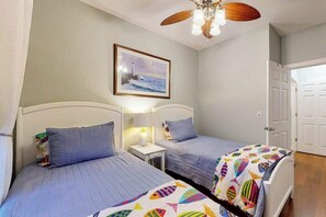 Ein Zimmer mit zwei Betten, einem Deckenventilator, einem gerahmten Bild an der Wand und einer Tür.