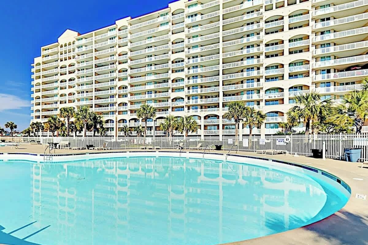 Un hôtel doté d’une grande piscine, de nombreux balcons et de palmiers.