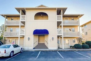 A multi-story building with a central entrance, a covered porch, and a parking lot. - Pinehurst Unit X-7 Condo (Little River)