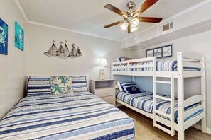 A bedroom with a bed, bunk beds, a ceiling fan, wall art, and a nightstand. - Waipani Unit A-18 Condo (North Myrtle Beach)
