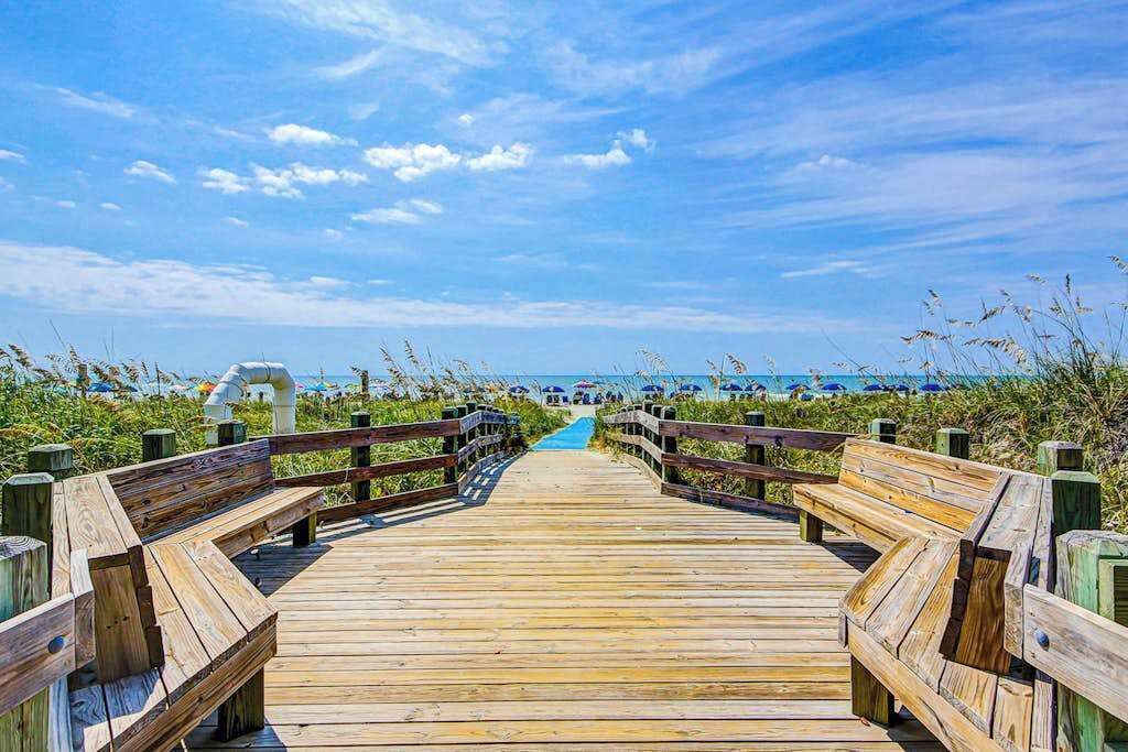 Une promenade en bois menant à une plage, avec un ciel dégagé.