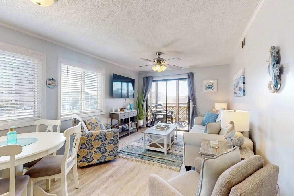 Un vaste salon doté d’un ventilateur de plafond, un coin repas avec une table et des chaises, et un espace détente avec un canapé et des fauteuils.
