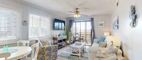 Amplia sala de estar con ventilador de techo, comedor con mesa y sillas, y zona de estar con sofá y sillones.