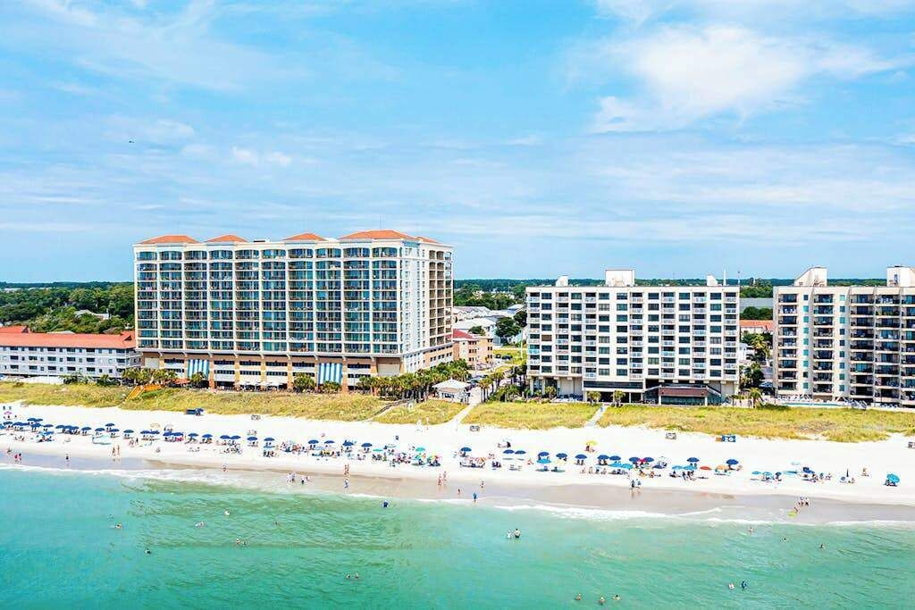 A beachfront hotel with multiple high-rise buildings, a sandy beach, and clear blue waters.
